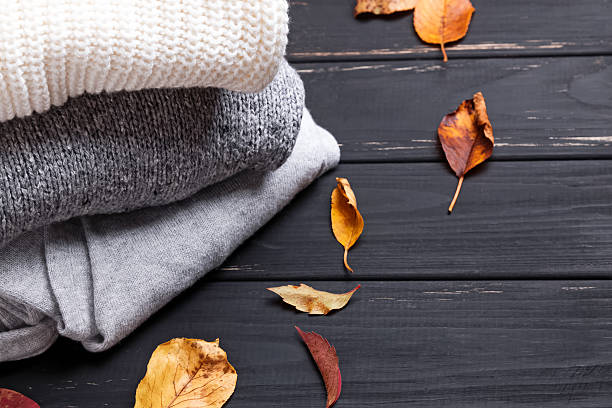 Cozy sweaters and autumn leaves on thw black wooden background
